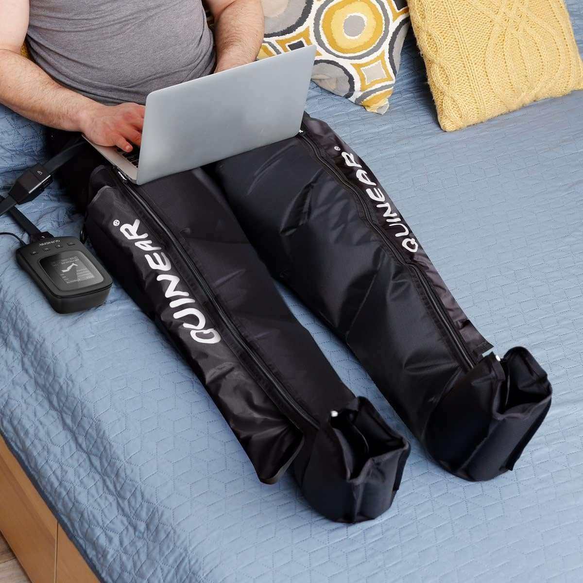 Person using black Air Compression Massage System leg recovery boots with control unit on bed