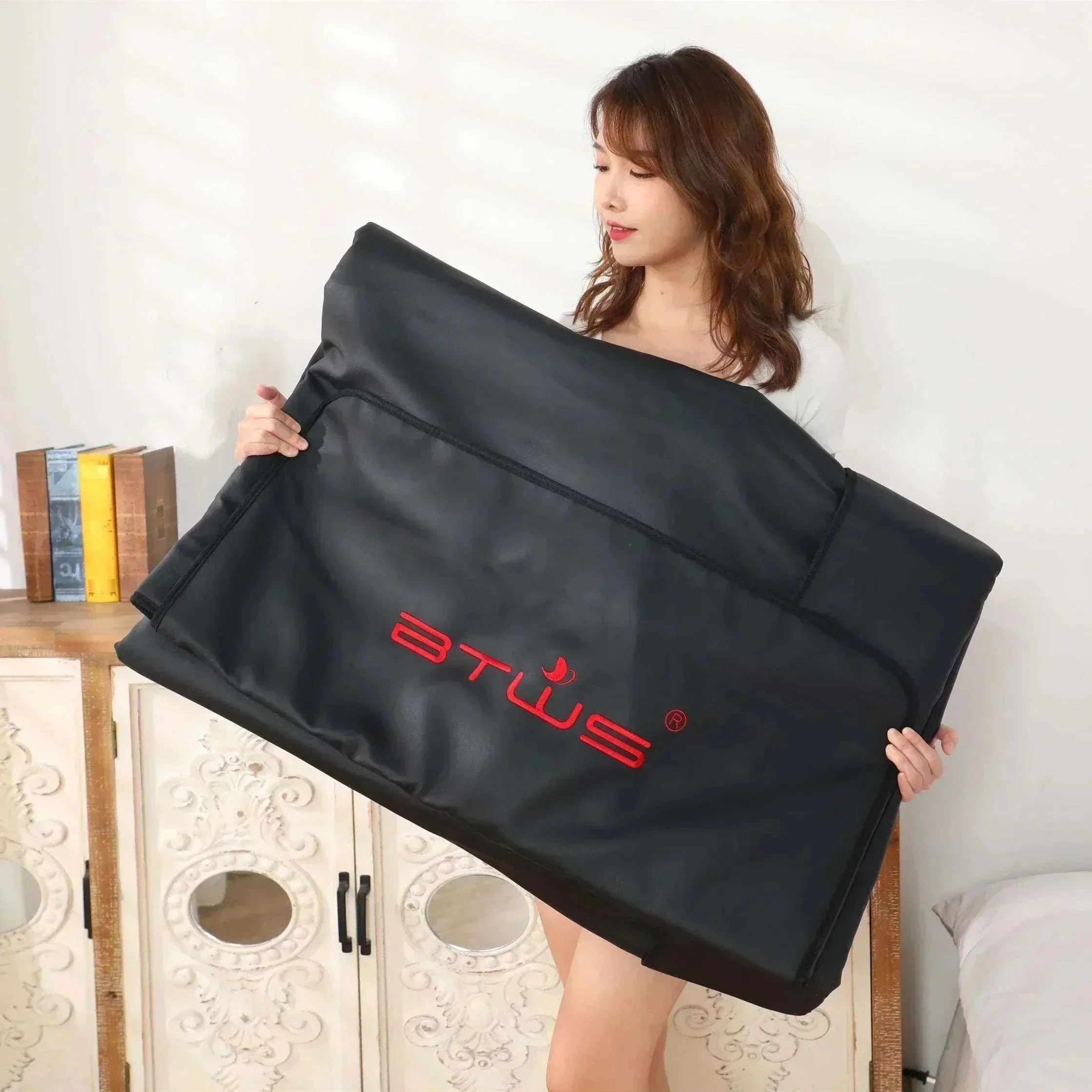 Woman holding black foldable infrared sauna blanket for weight loss and detox at home